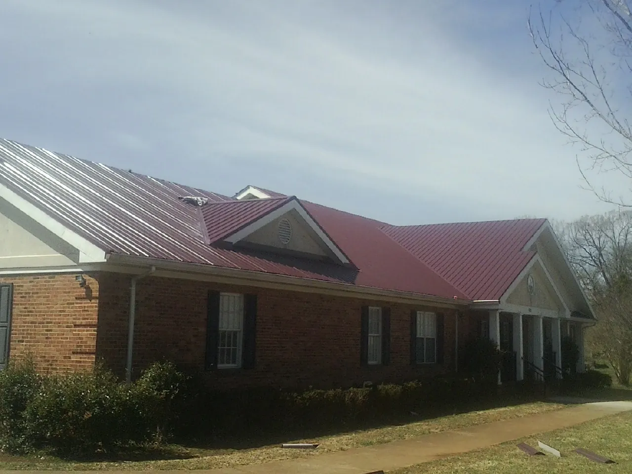 Red metal roof with gabled entries on a long brick building, from a Hail Damage Roof Repair job in Worcester