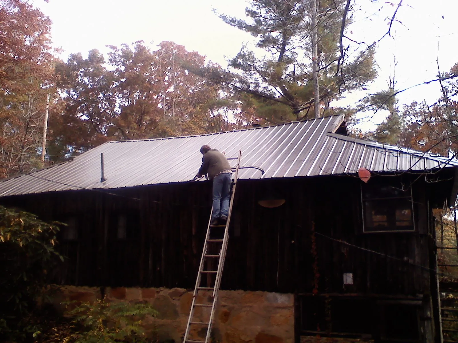 Roofer on a ladder working along the edge of a cabin metal roof in Worcester
